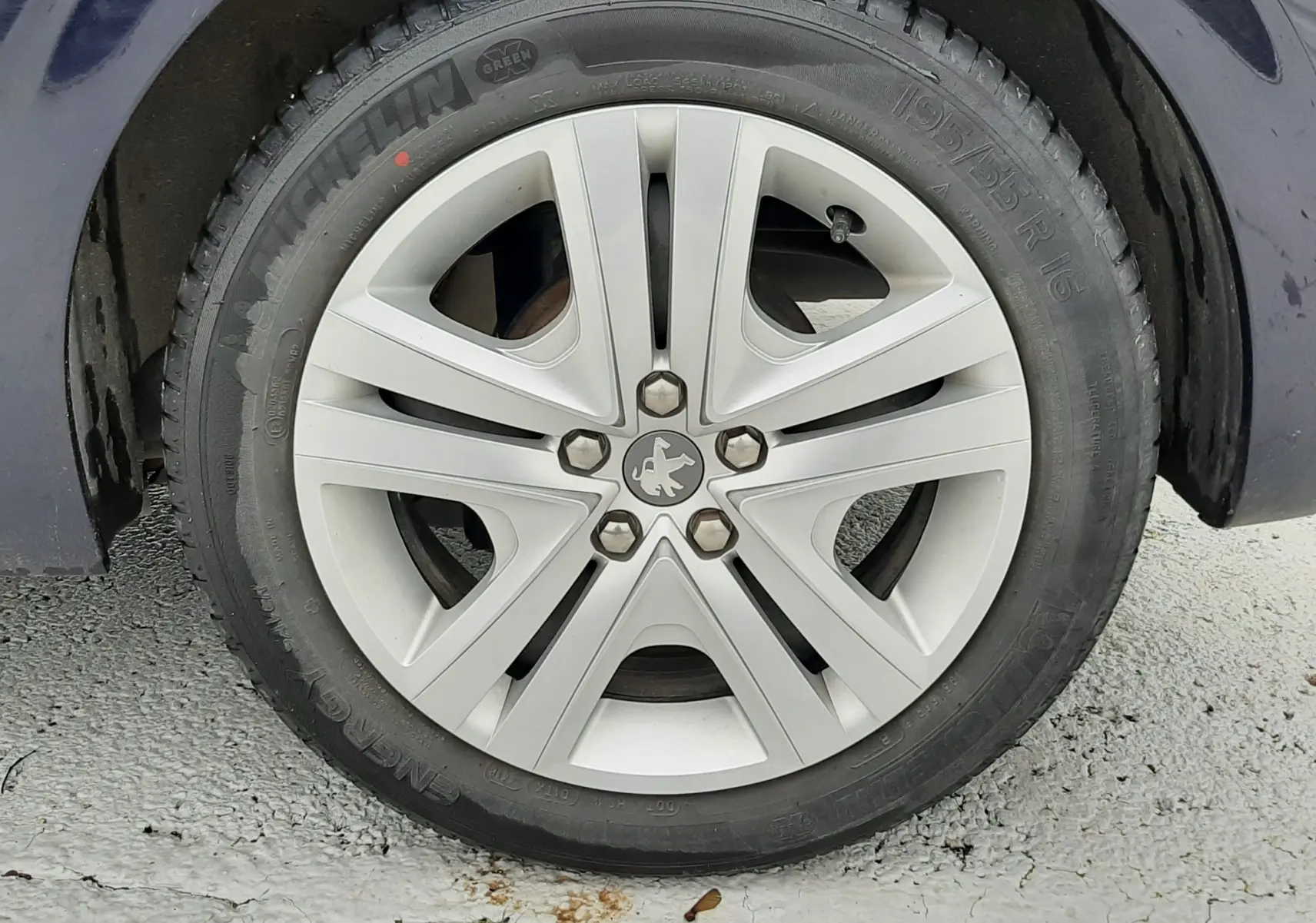 Gros plan sur la roue avant gauche d'une Peugeot 208 bleu nuit avec jante alliage cinq branches.