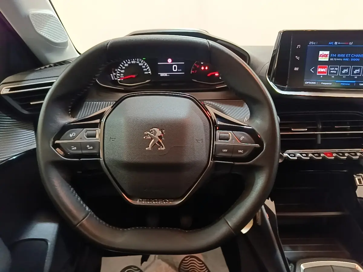 Vue rapprochée du volant cuir noir et du tableau de bord numérique de la Peugeot 208 gris clair 2023.