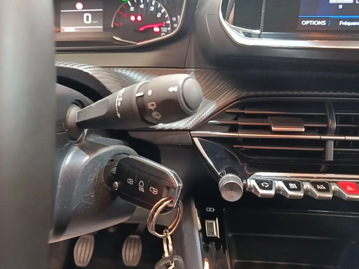Gros plan intérieur sur le tableau de bord de la Peugeot 208 gris clair, clé insérée et commandes centrales visibles.