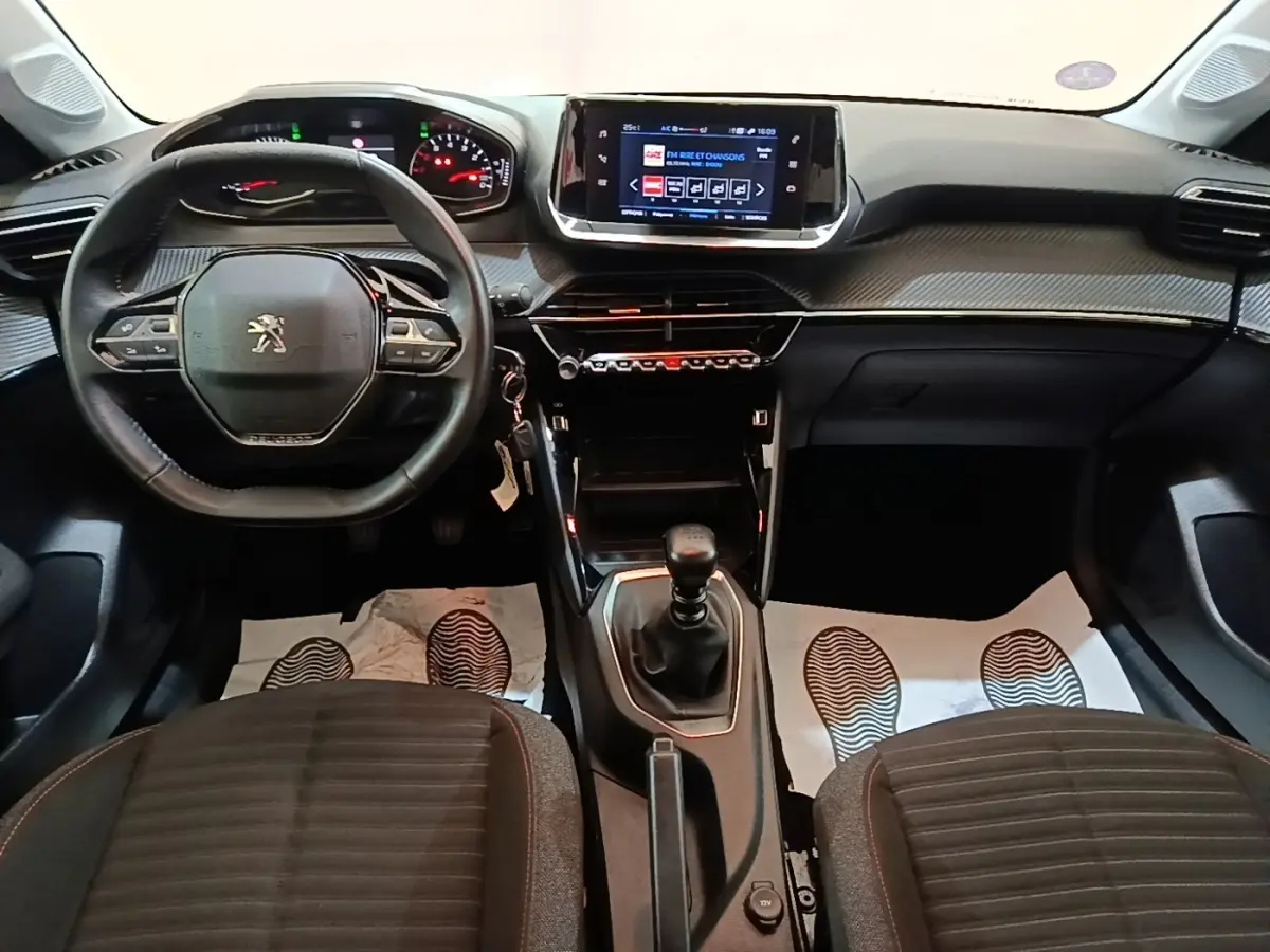 Vue intérieure avant du Peugeot 208 2023 avec volant cuir multifonctions, écran tactile central et boîte manuelle.
