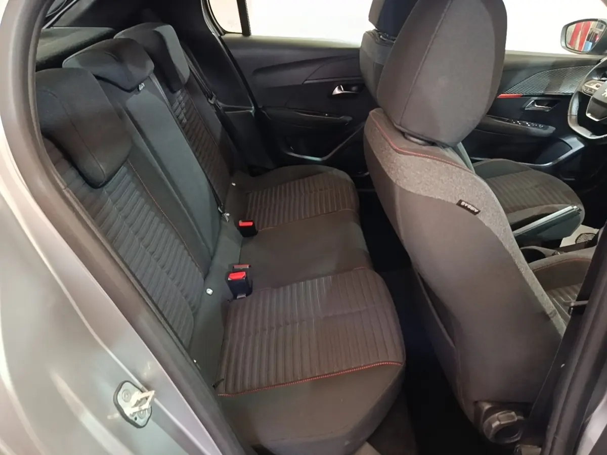 Vue intérieure côté arrière droit de la Peugeot 208 gris clair, montrant la banquette arrière noire avec surpiqûres rouges.