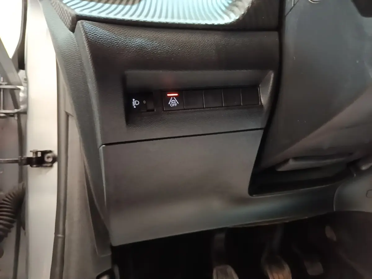 Vue rapprochée du tableau de bord côté conducteur d'une Peugeot 208 gris clair, avec boutons de réglage des phares et assistance au maintien de voie.