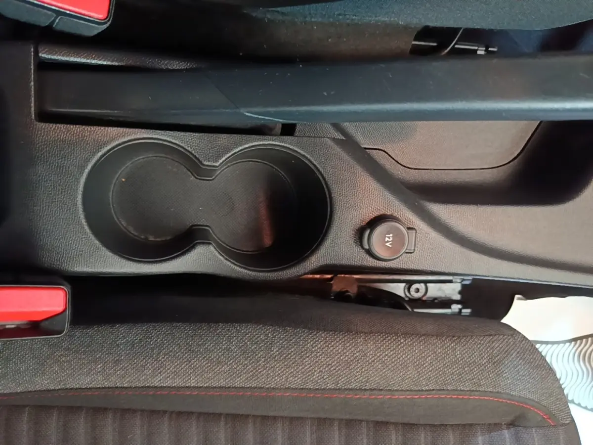 Gros plan sur la console centrale noire avec porte-gobelets et prise 12V dans une Peugeot 208 gris clair.
