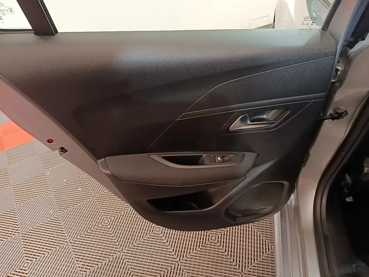 Vue rapprochée de la porte arrière droite grise claire du Peugeot 208 2023, avec poignée et commande de vitre noire.