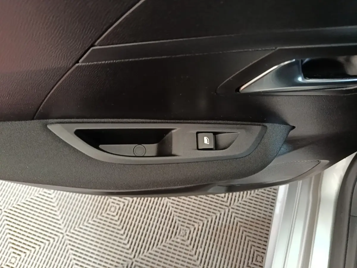 Détail de la porte avant gauche d’une Peugeot 208 gris clair, avec bouton de verrouillage et poignée intérieure chrome.