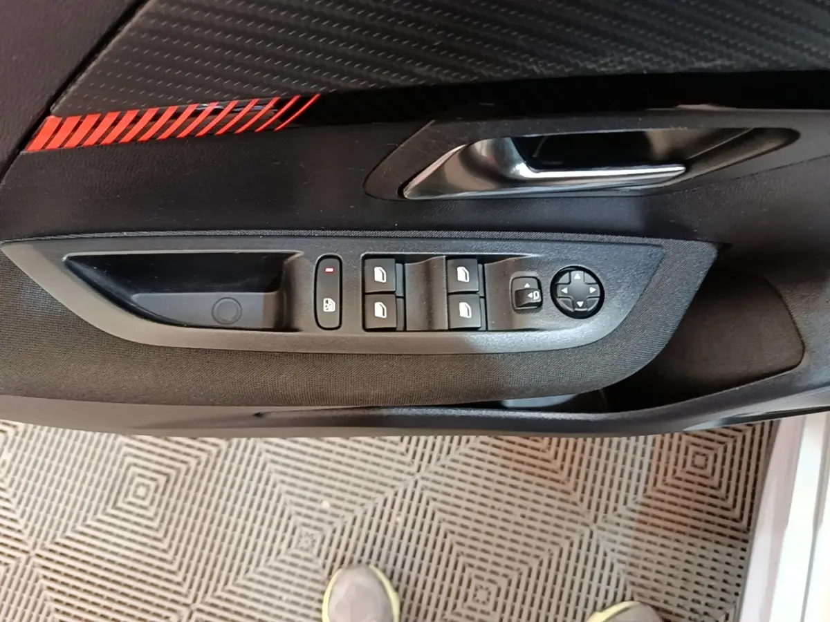 Vue rapprochée de la porte côté conducteur d'une Peugeot 208 2023, montrant les commandes des vitres et rétroviseurs.