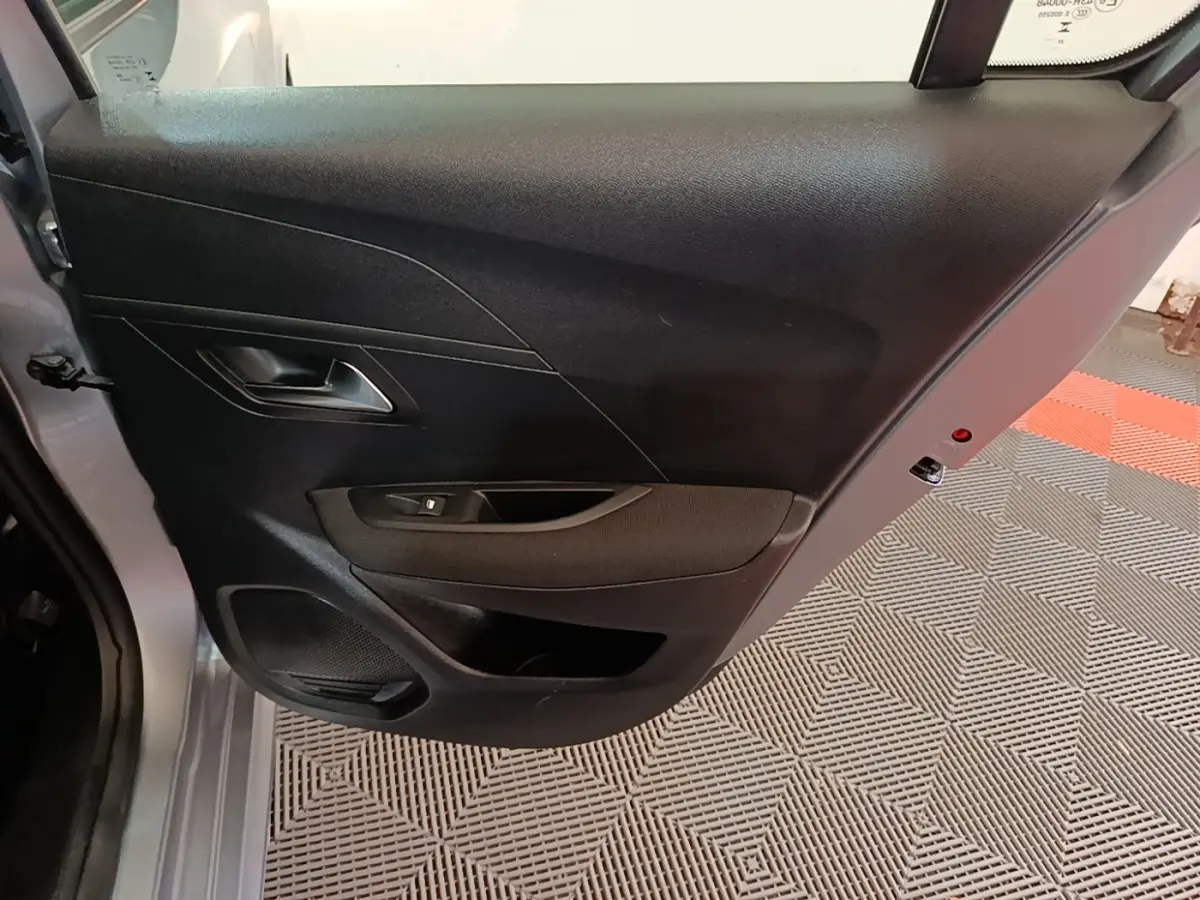 Vue rapprochée de la porte arrière gauche gris clair d’une Peugeot 208 2023 avec panneau intérieur noir et commande de vitre.
