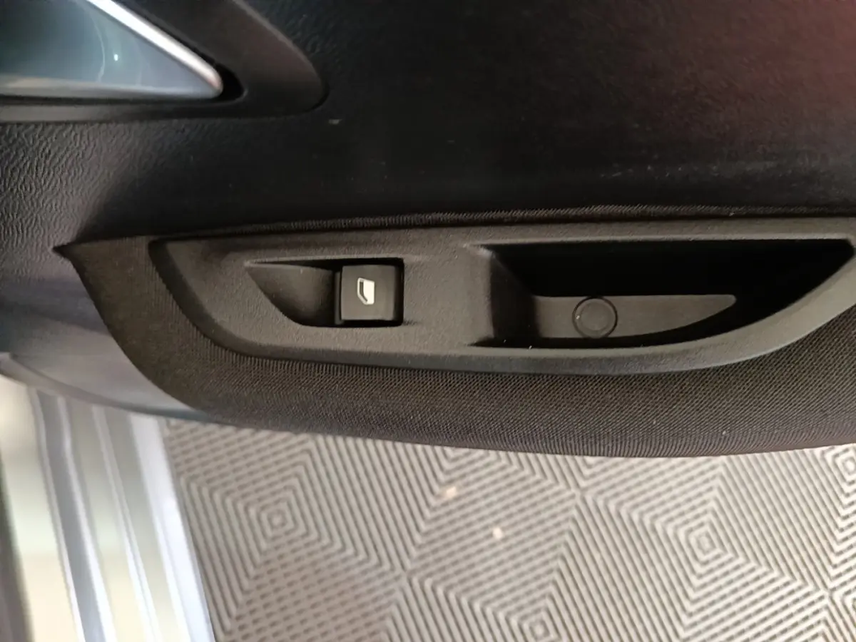 Détail de la commande de lève-vitre sur la porte intérieure côté conducteur d’une Peugeot 208 gris clair 2023.