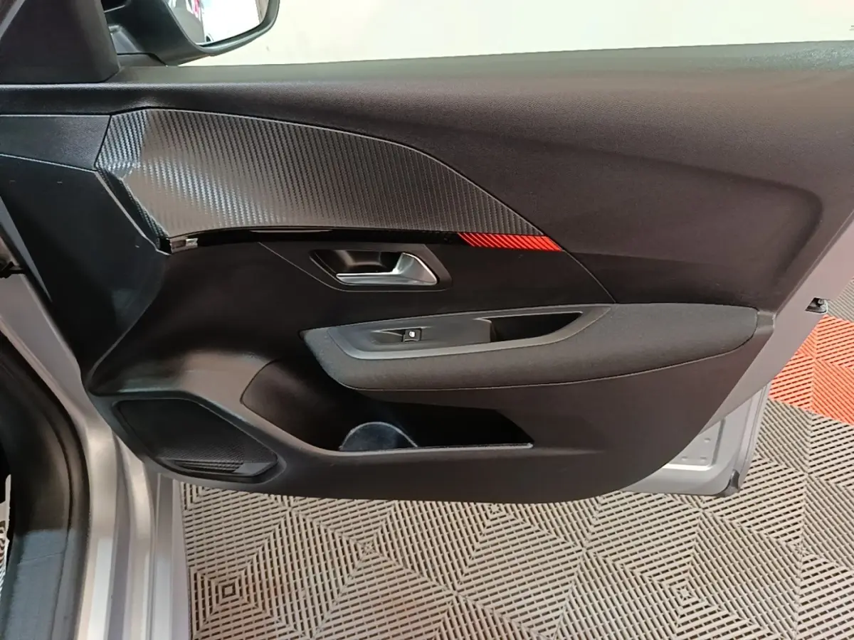 Vue intérieure de la porte avant gauche du Peugeot 208 gris clair, avec insert carbone et bande rouge décorative.