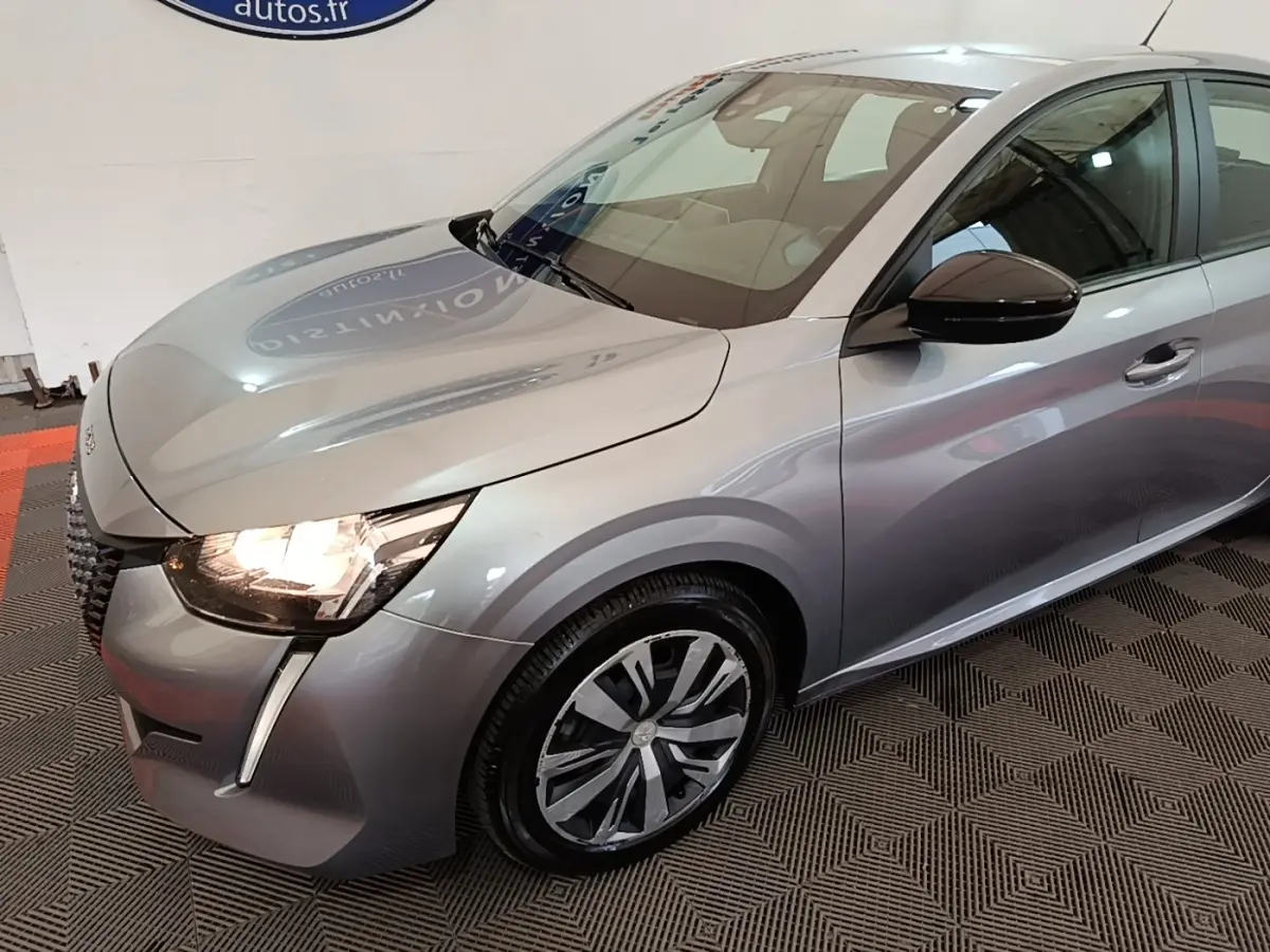 Peugeot 208 gris clair vue 3/4 avant droit avec phares allumés et jantes alliage distinctives.