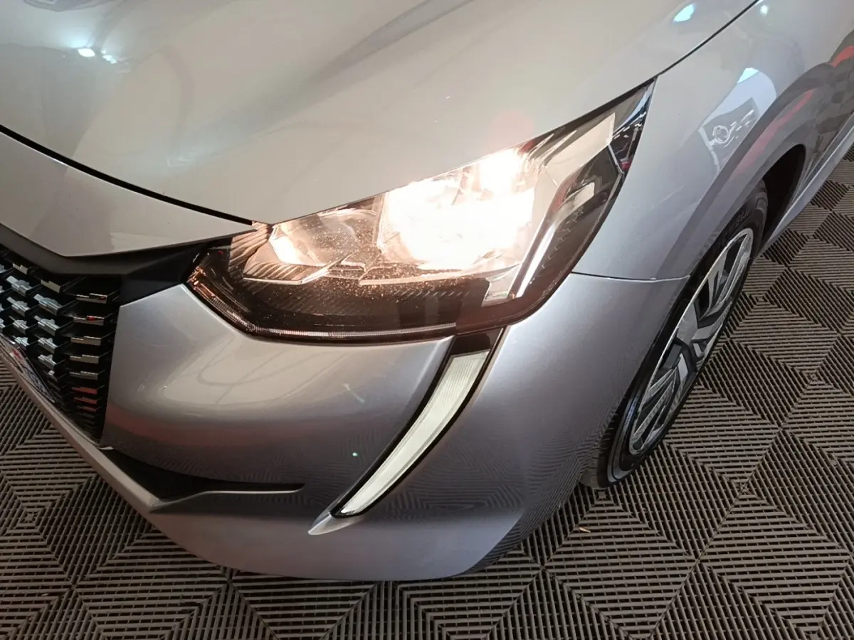 Gros plan sur l'avant droit gris clair de la Peugeot 208 2023 avec phare allumé et jante visible.