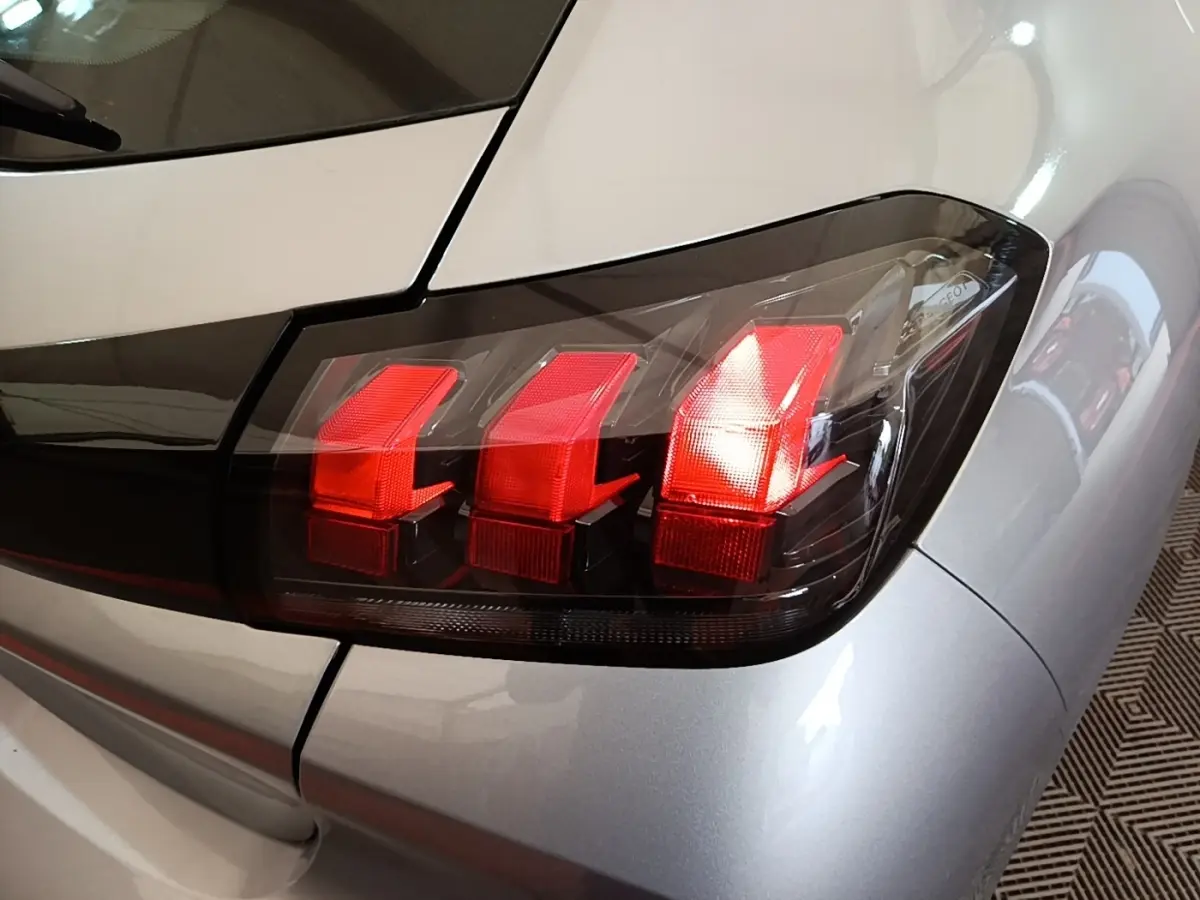 Gros plan sur le feu arrière droit rouge d’une Peugeot 208 gris clair, version PureTech 100 S&S Active Pack 2023.