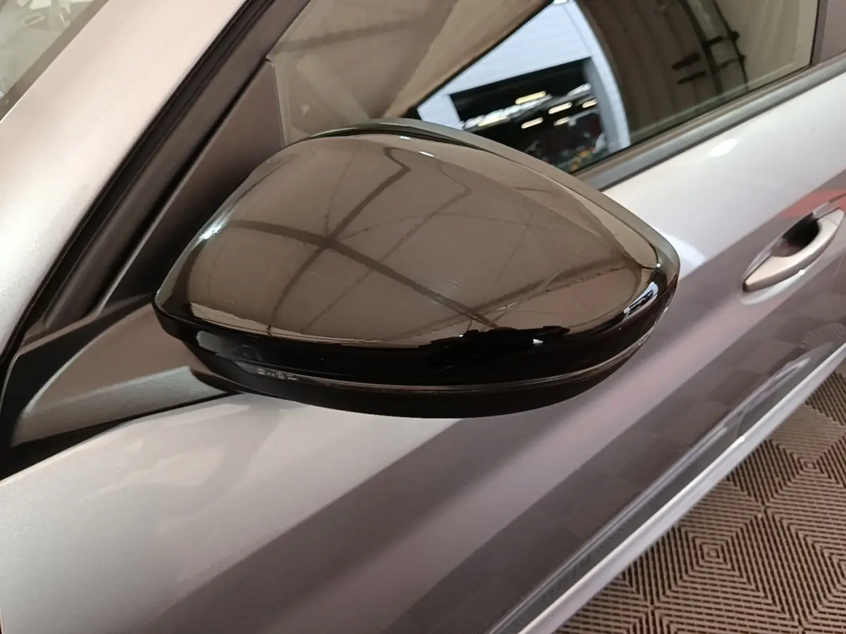 Gros plan sur le rétroviseur noir brillant côté conducteur d’une Peugeot 208 gris clair, vue de profil.