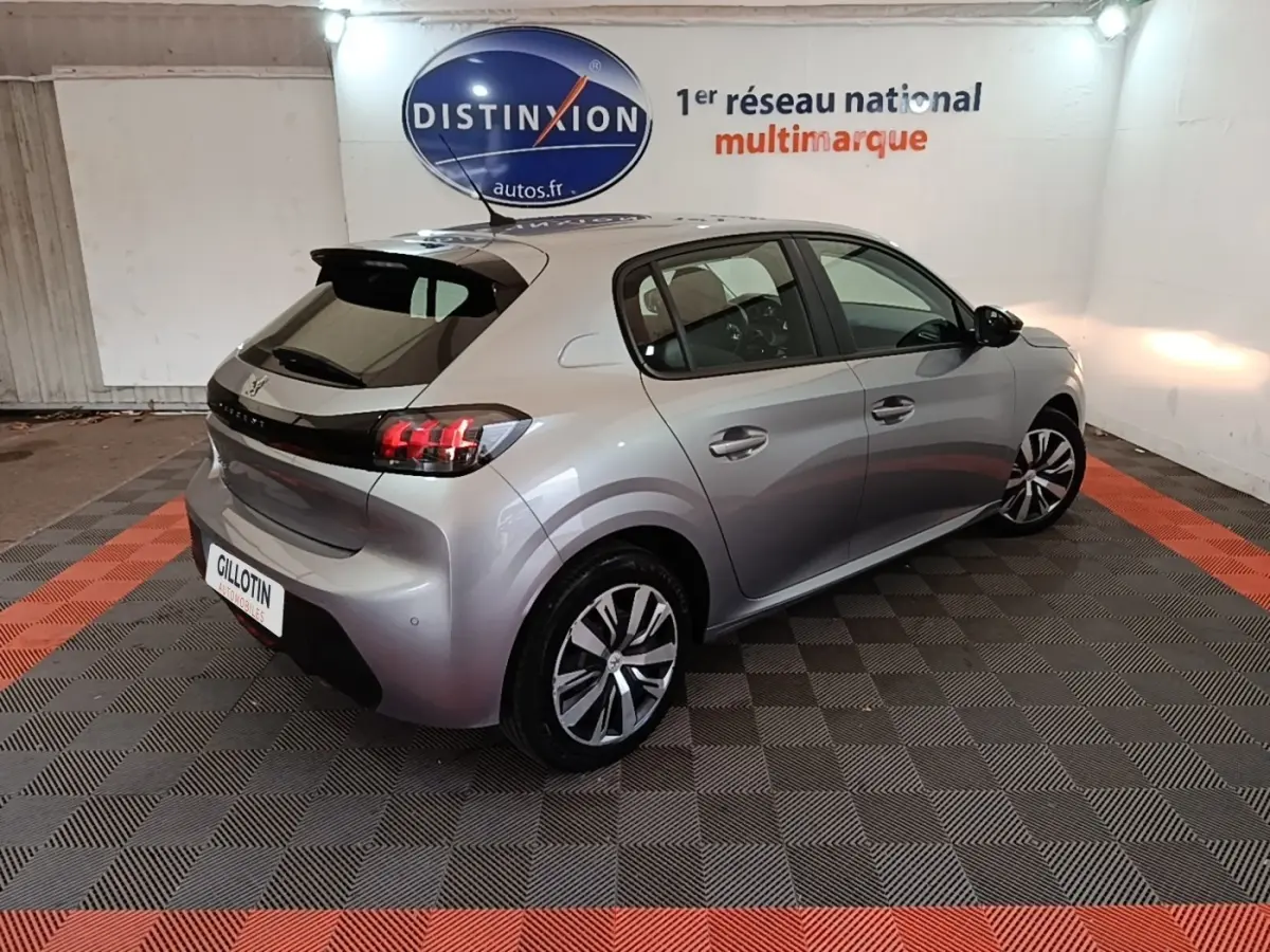 Peugeot 208 gris clair vue 3/4 arrière droit en intérieur, feux arrière LED et jantes alliage visibles.