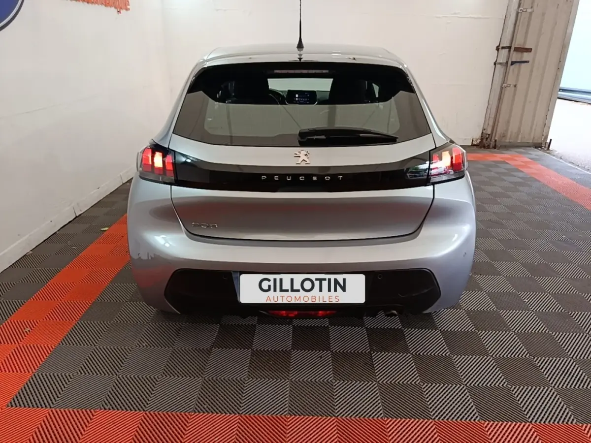 Vue arrière d'une Peugeot 208 gris clair 2023 avec feux LED et logo Peugeot sur bande noire brillante.