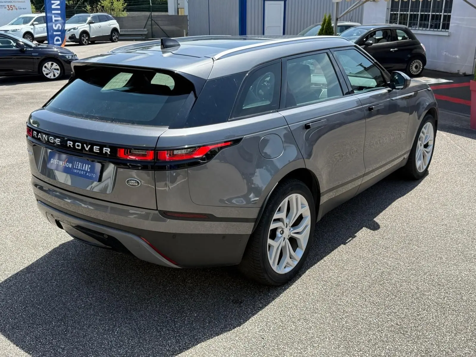 Vue 3/4 arrière droite d'un Range Rover Velar gris métallisé avec jantes blanches et feux arrière LED distinctifs.
