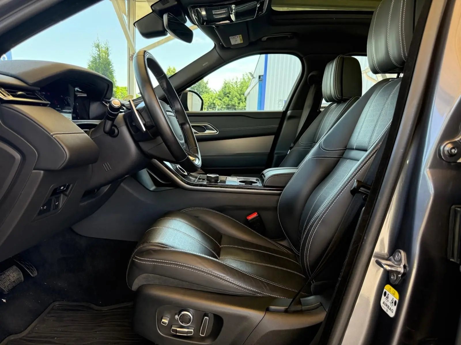 Intérieur côté conducteur du Range Rover Velar gris 2019, sièges en cuir noir avec surpiqûres blanches et tableau de bord moderne.