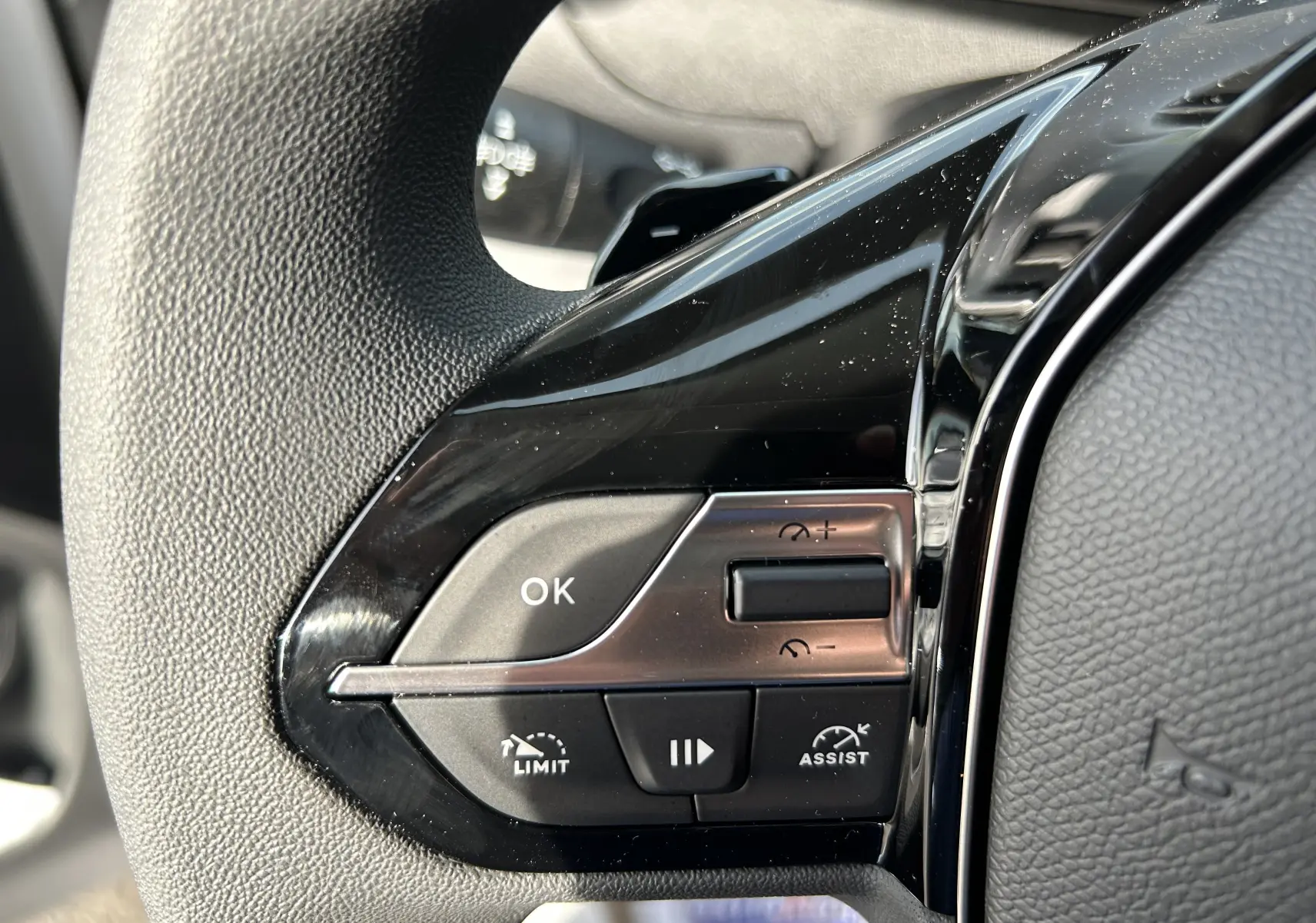 Gros plan sur les commandes noires du volant du Peugeot Partner Fourgon blanc, avec boutons de limitation et assistance.