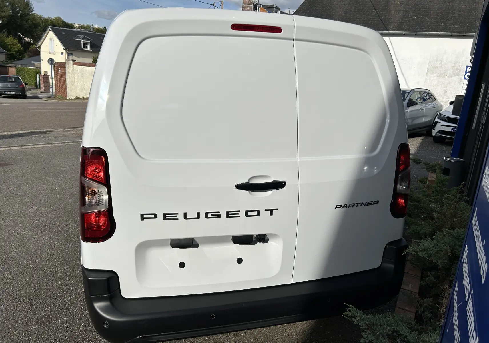 Vue arrière d'un utilitaire Peugeot Partner blanc avec portes battantes et feux arrière rouges.