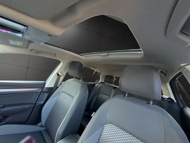 Vue intérieure avant de la Volkswagen Golf VIII gris lunaire, avec toit panoramique ouvert et sièges tissu gris.