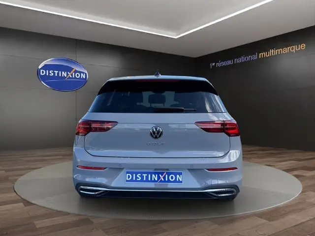 Vue arrière d'une Volkswagen Golf VIII gris lunaire avec toit panoramique et feux LED, en intérieur showroom.