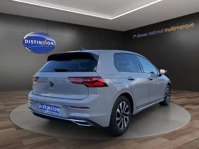 Volkswagen Golf VIII gris lunaire vue 3/4 arrière droit en intérieur avec jantes alu et vitres surteintées.