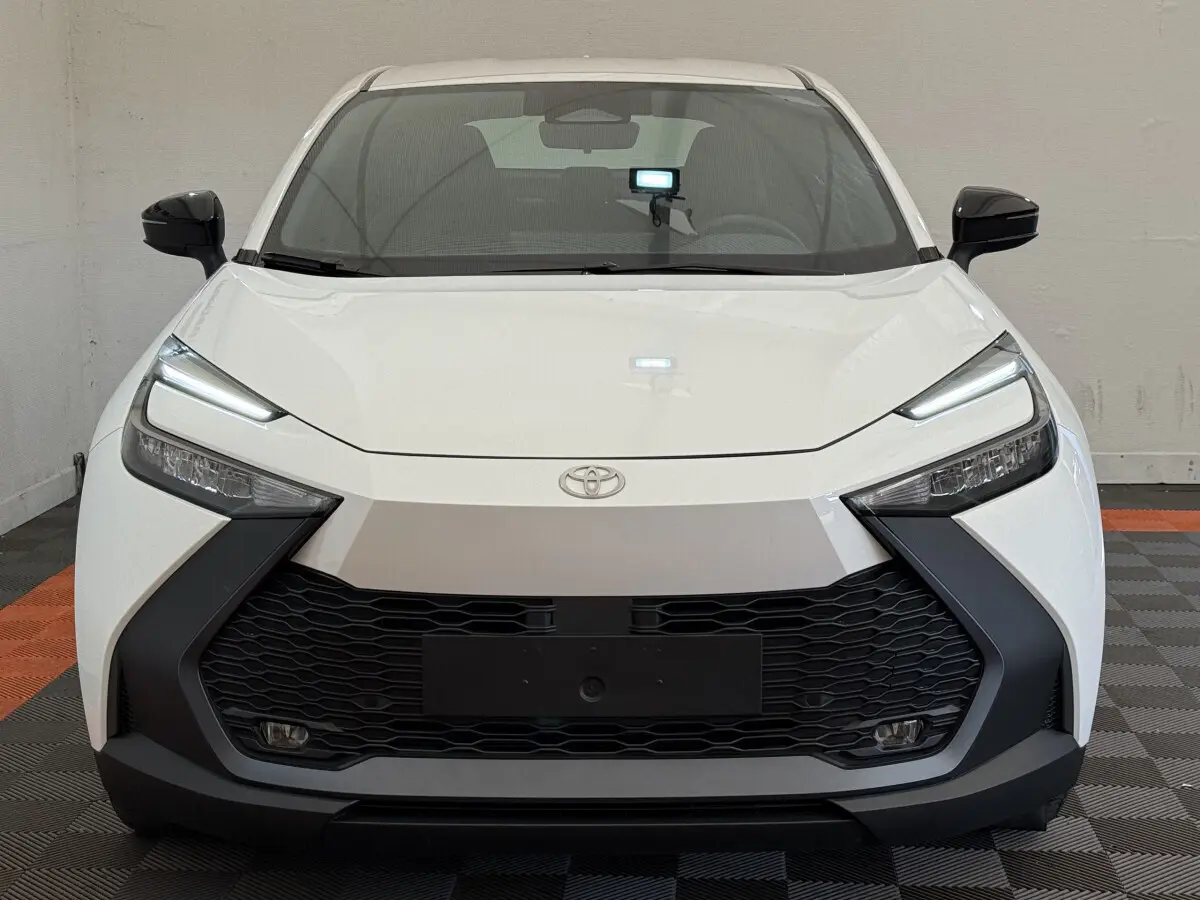 Vue frontale du Toyota C-HR 1.8 Hybride blanc avec calandre noire et phares LED fins allumés.