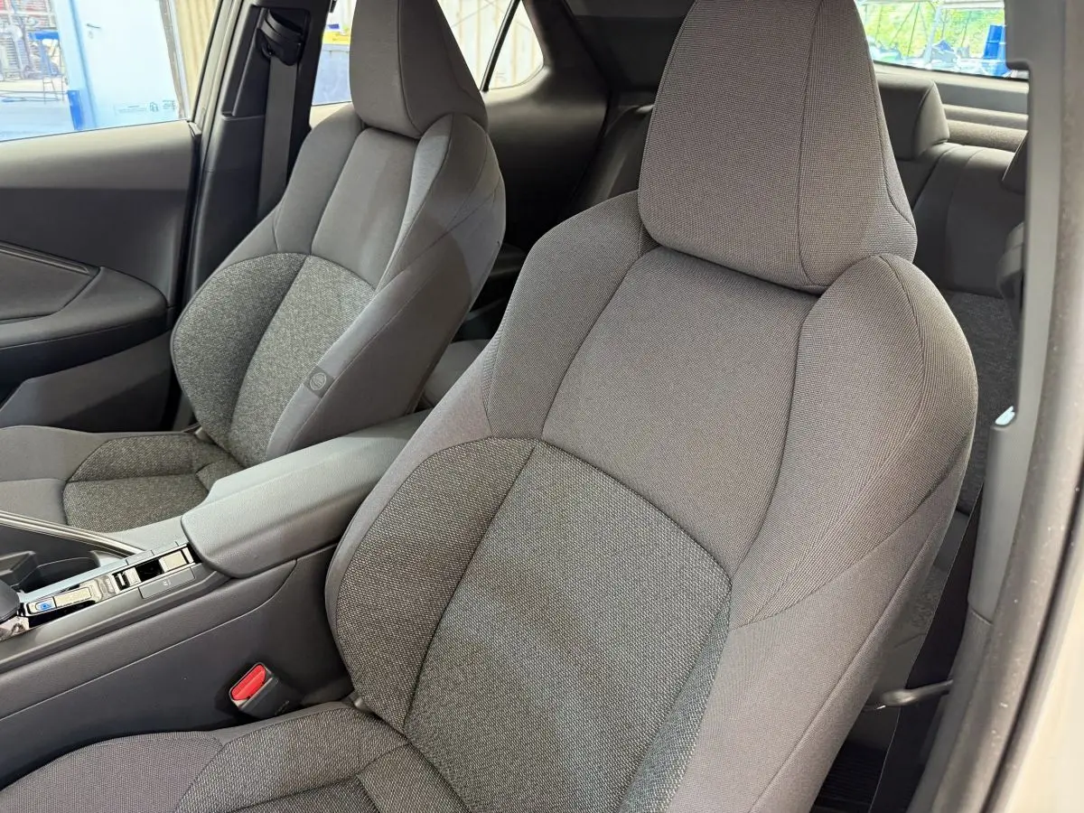 Vue intérieure rapprochée des sièges avant gris du Toyota C-HR 1.8 Hybride 140 Dynamic blanc, avec accoudoir central.