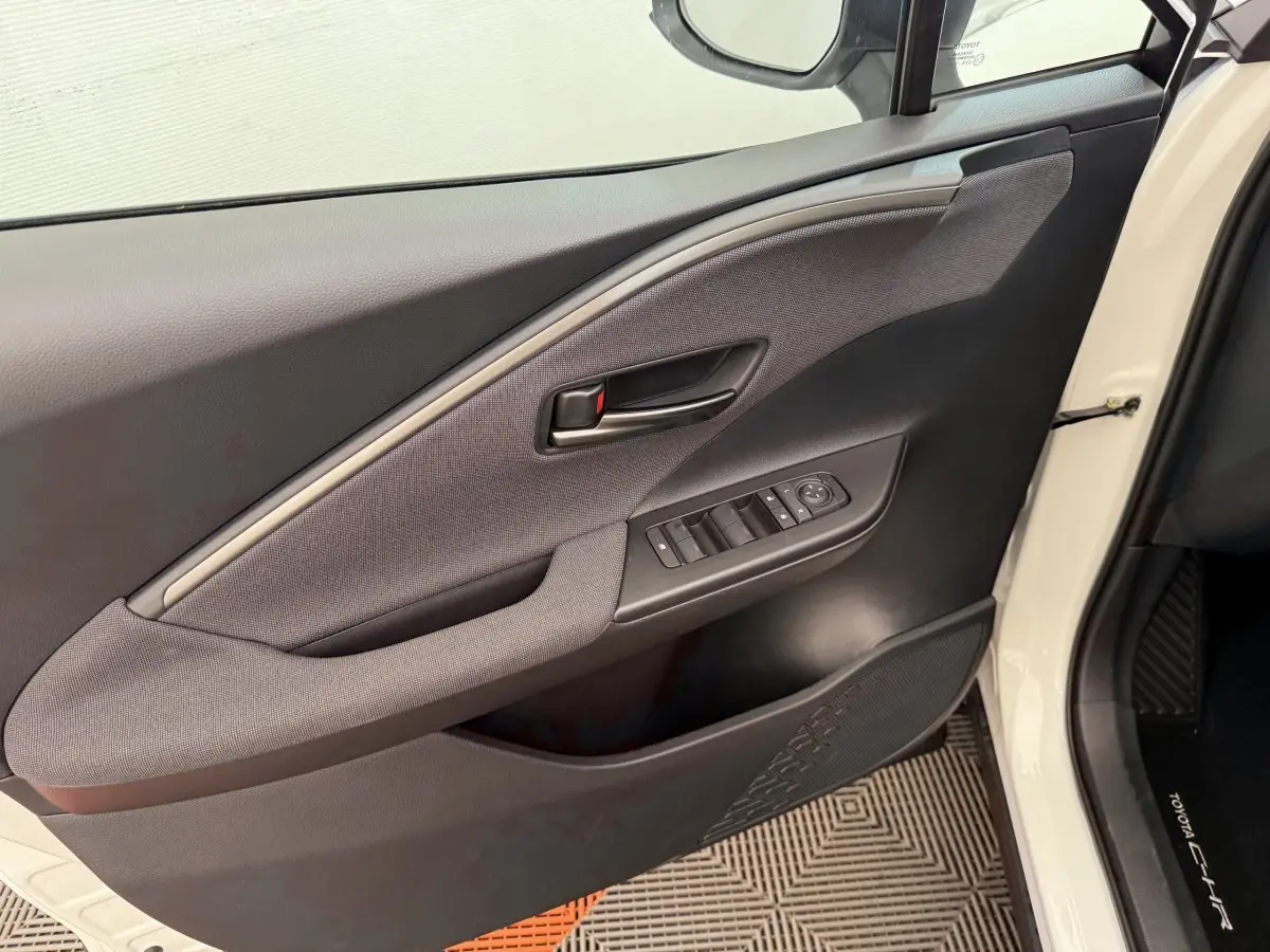 Vue intérieure côté gauche de la porte avant blanche du Toyota C-HR 1.8 Hybride avec commandes de vitres et poignée noire.