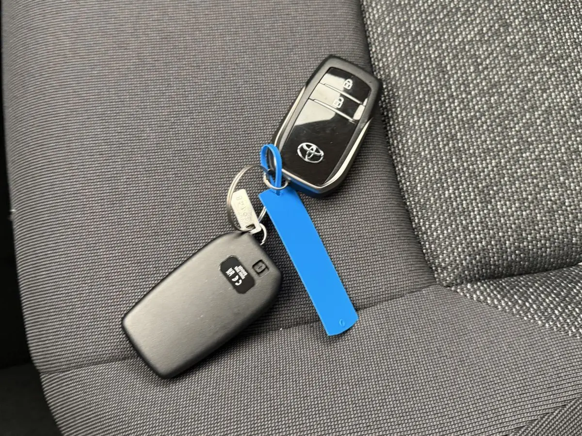 Gros plan sur la clé noire Toyota posée sur un siège tissu gris foncé, avec un porte-clés bleu visible.