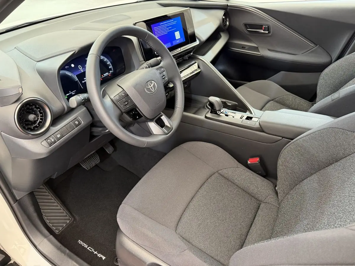 Intérieur avant droit du Toyota C-HR blanc 2024, volant cuir, écran tactile et sièges tissu gris.
