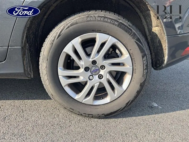 Gros plan sur la roue avant droite d'un Volvo XC60 gris Savile avec jante alu distinctive et pneu toutes saisons.