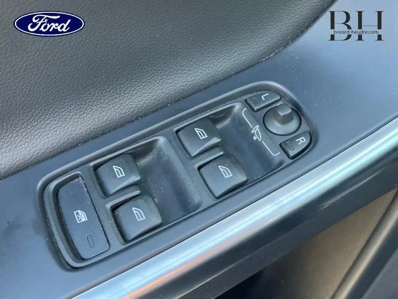 Gros plan sur les commandes de lève-vitres et rétroviseurs côté conducteur d'un Volvo XC60 gris Savile, intérieur noir.