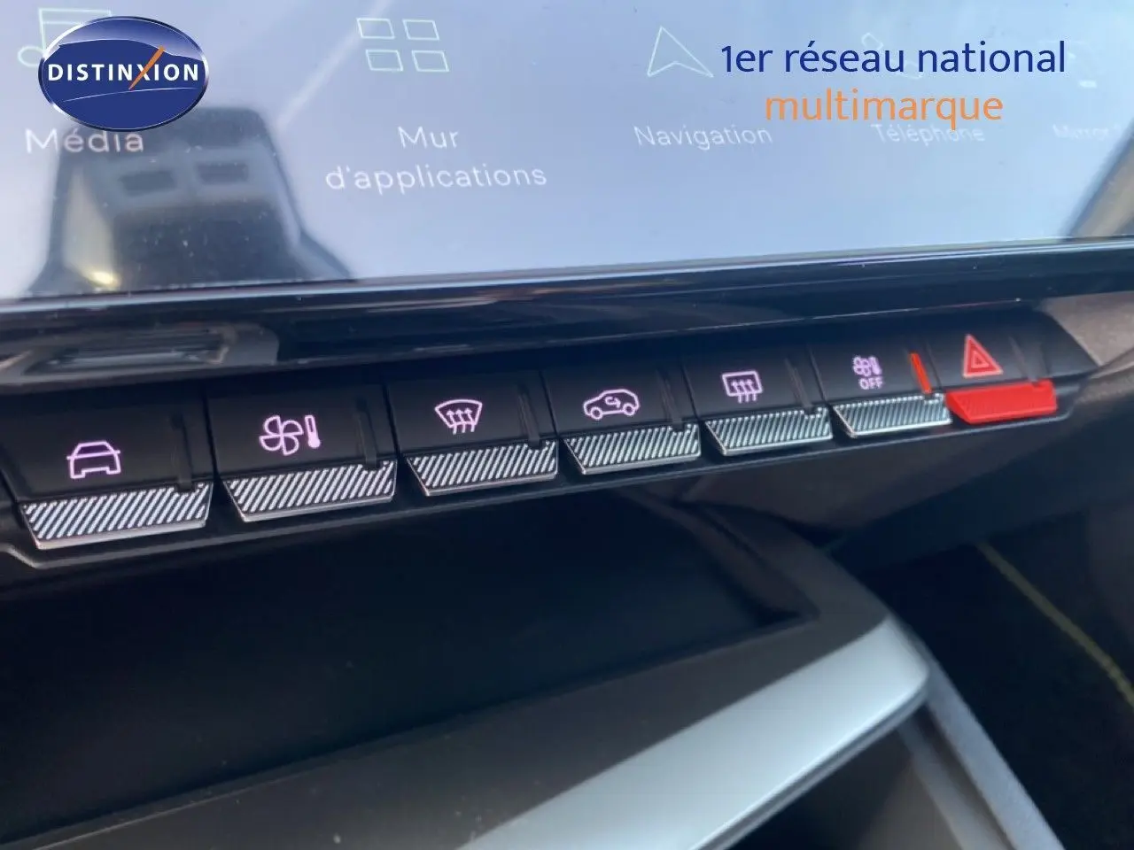 Gros plan sur la rangée de boutons tactiles du tableau de bord de la Peugeot 308 blanche, avec éclairage violet et bouton rouge d'alerte.