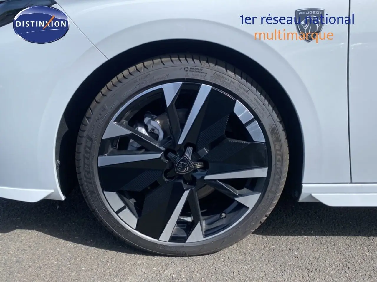 Gros plan sur la roue avant gauche de la Peugeot 308 blanche Okenite Metal avec jante alliage noire et argentée au design moderne.