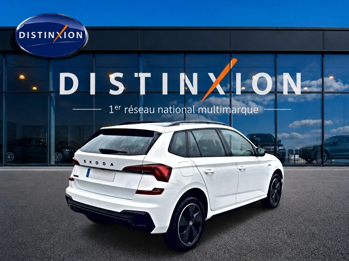 Vue 3/4 arrière droite d'un Skoda Kamiq blanc nacré avec jantes noires devant une vitrine Distinxion.