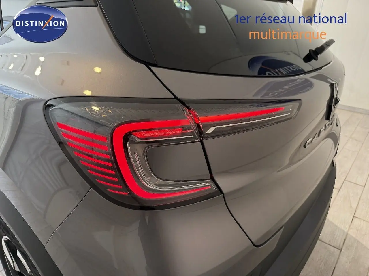Gros plan sur le feu arrière gauche rouge d’un Renault Captur gris cassiopée métal avec toit gris, vue arrière en intérieur.