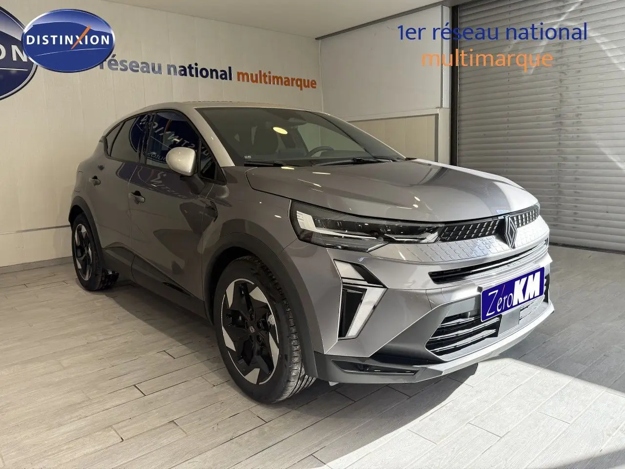 Renault Captur 2025 gris cassiopée métal avec toit gris, vu en 3/4 avant droit dans un showroom.
