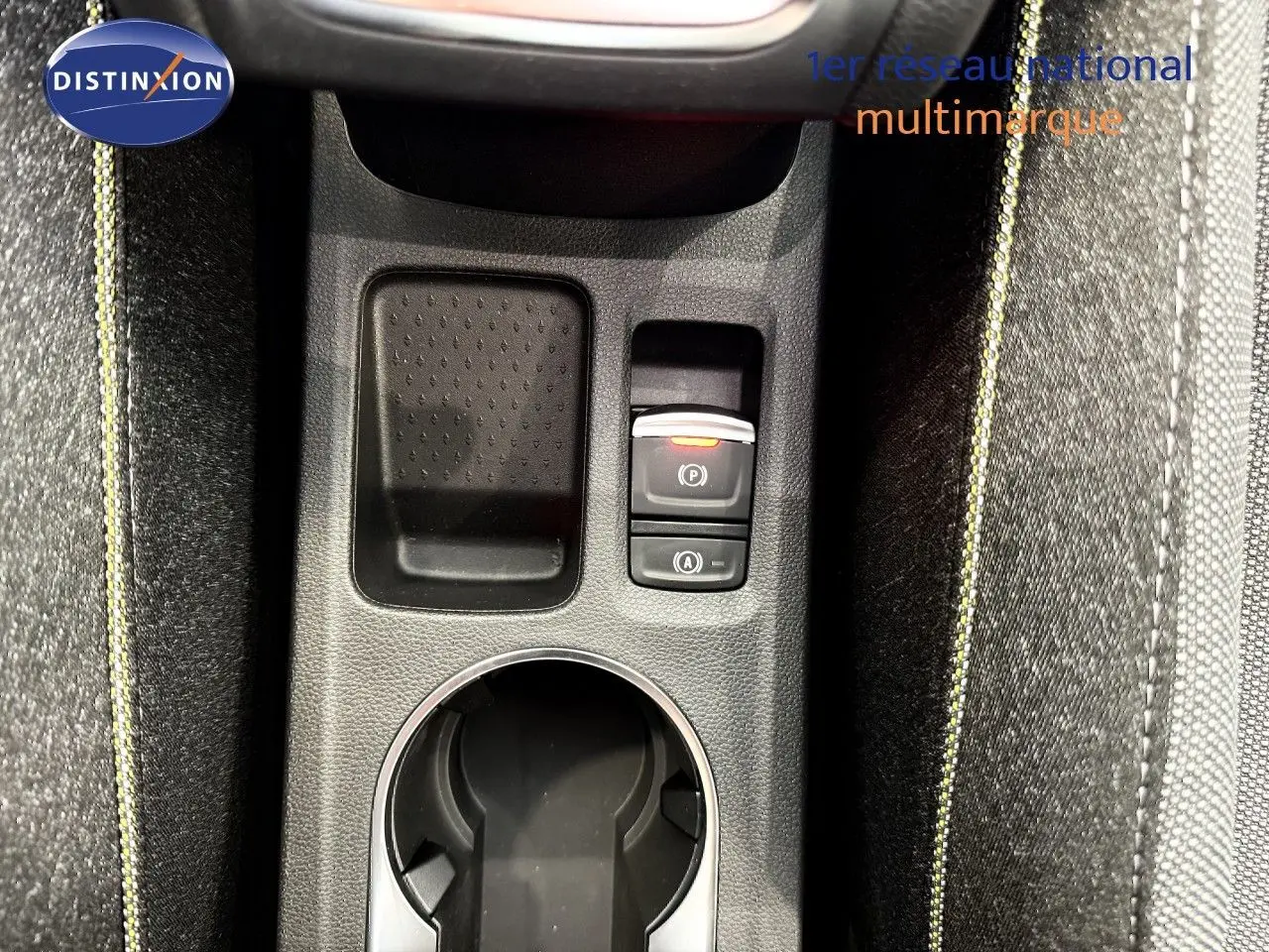 Vue rapprochée de la console centrale du Renault Captur gris cassiopée, avec bouton frein à main électronique et surpiqûres jaunes.