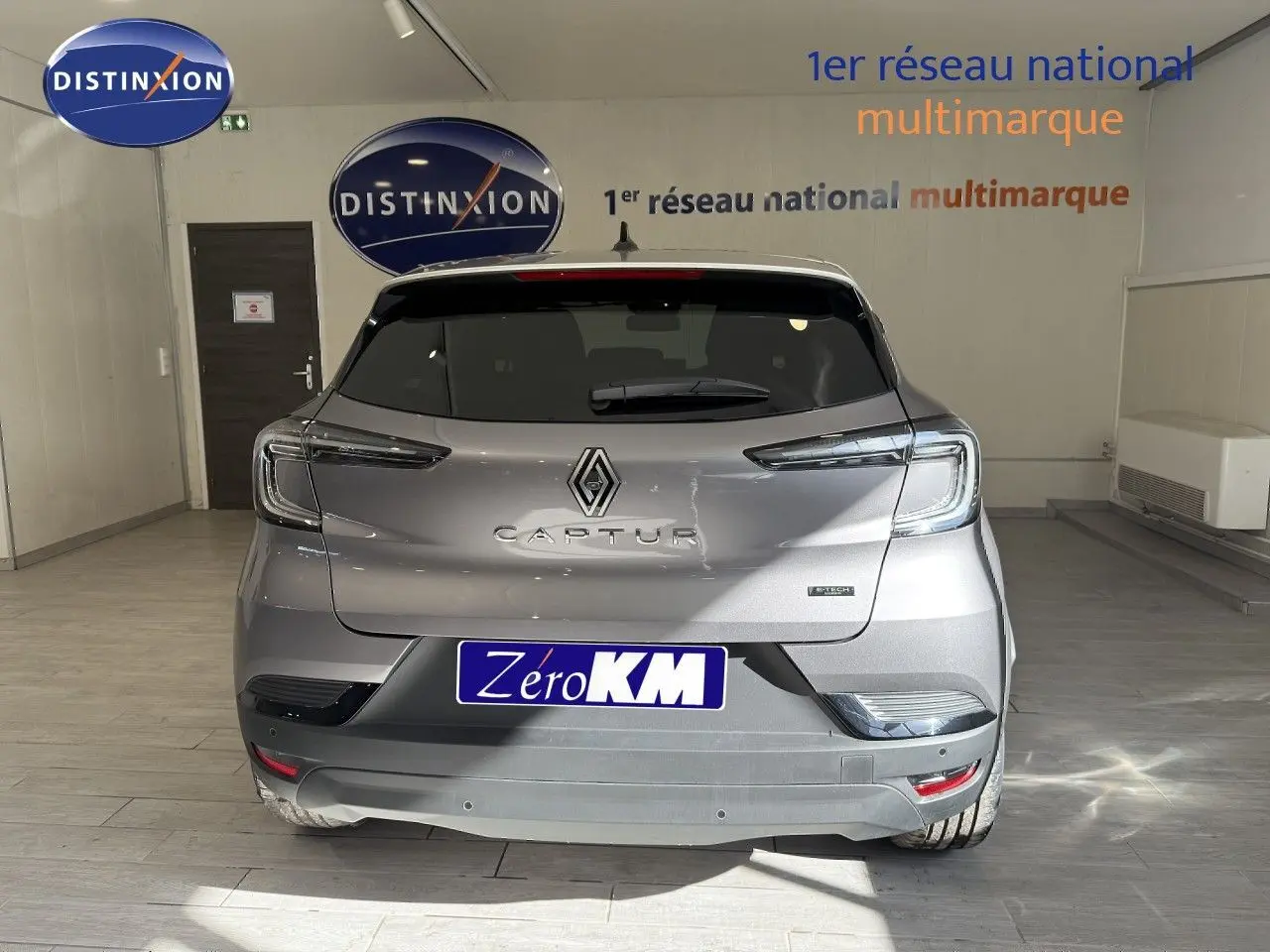 Vue arrière d'un Renault Captur gris Cassiopée métal avec toit gris, en intérieur showroom, badge hybride visible.