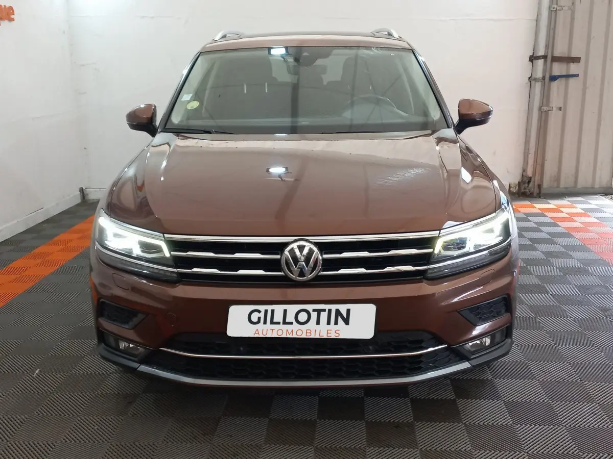 Vue frontale d'un Volkswagen Tiguan Allspace marron avec phares LED allumés dans un garage.