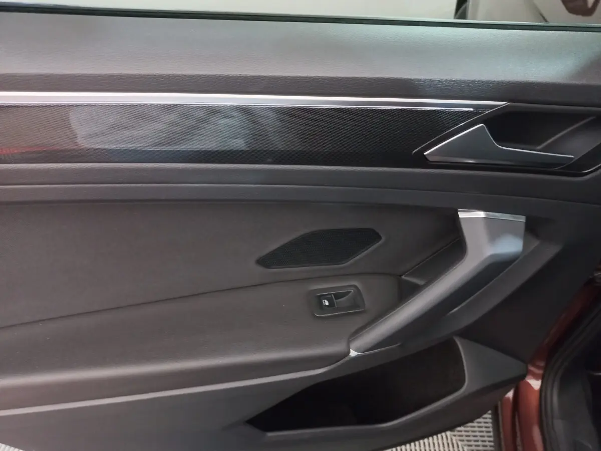 Gros plan sur la porte intérieure côté conducteur du Volkswagen Tiguan Allspace marron, avec poignée argentée et bouton de verrouillage.