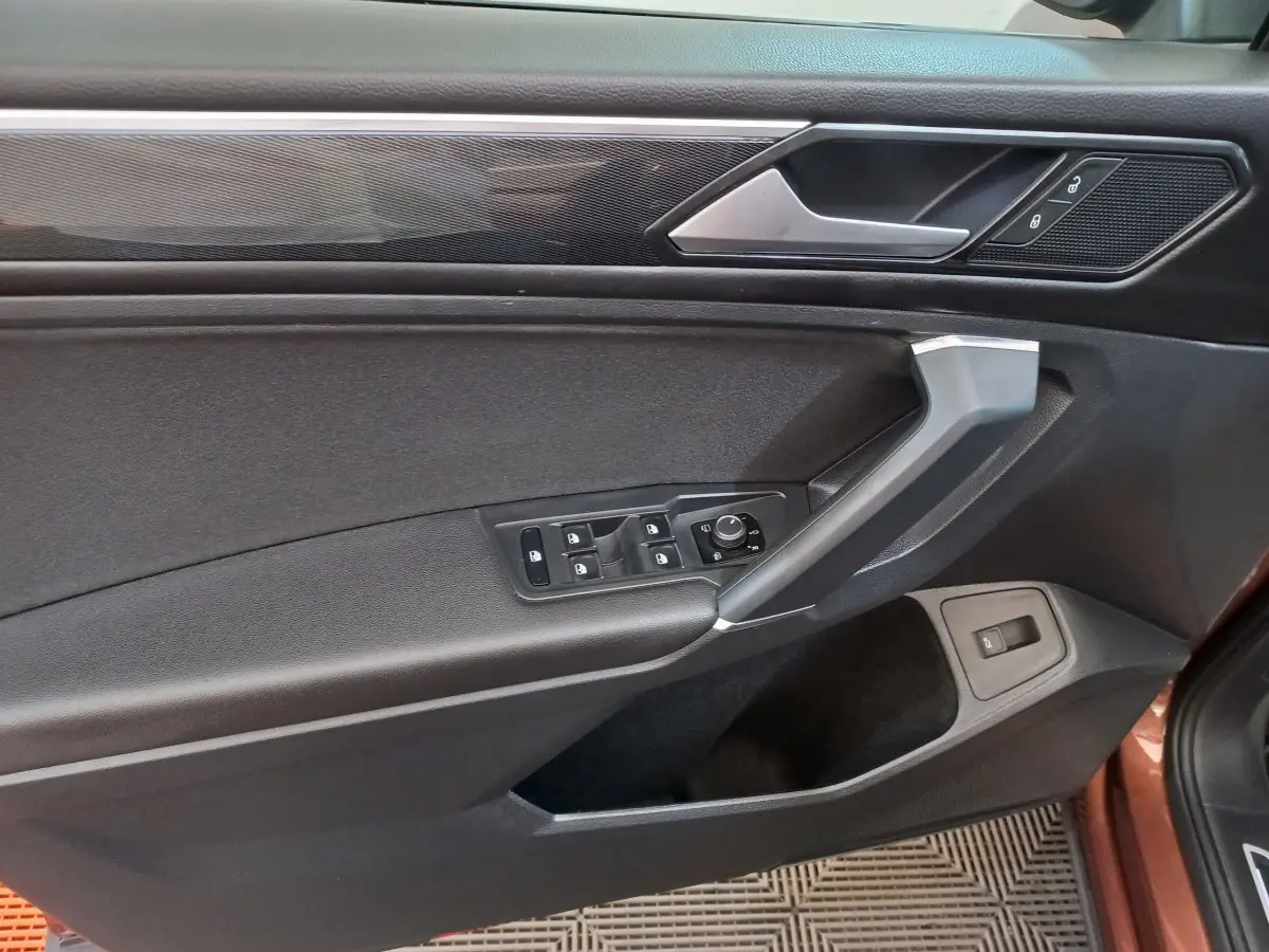 Vue intérieure côté gauche de la porte avant marron du Volkswagen Tiguan Allspace avec commandes vitres et rétroviseurs.