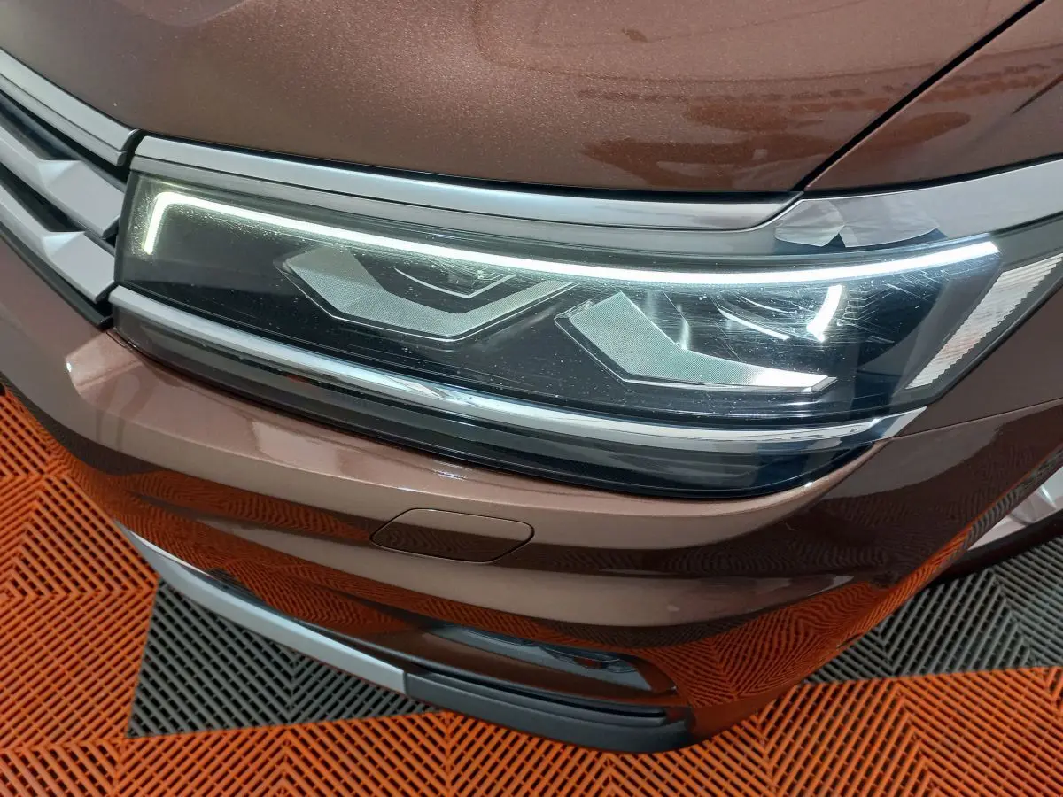 Gros plan sur le phare avant droit LED du Volkswagen Tiguan Allspace marron, avec calandre et pare-chocs visibles.