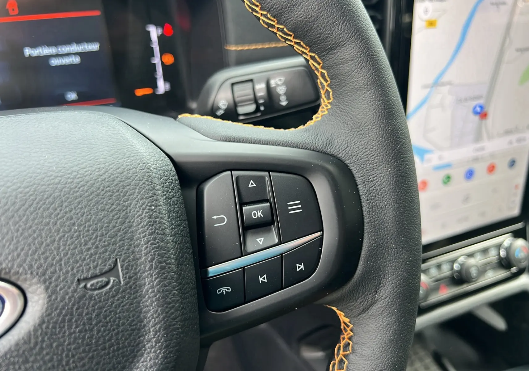 Gros plan sur le volant cuir noir avec surpiqûres orange du Ford Ranger 2025, montrant les commandes multifonctions et l’écran tactile GPS.