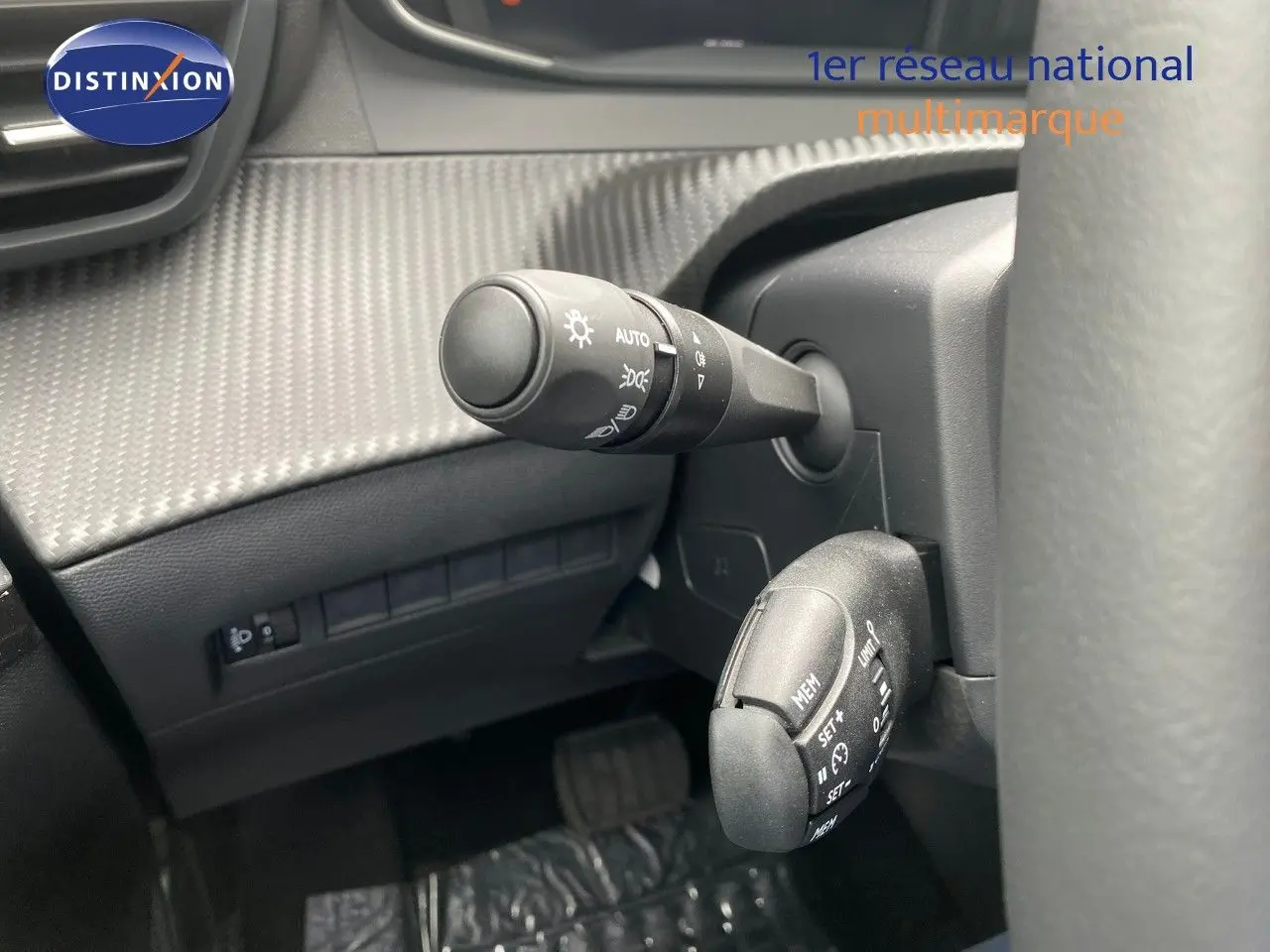 Détail intérieur montrant les commandes au volant et la texture carbone sur le tableau de bord d'une Peugeot 208 gris selenium.