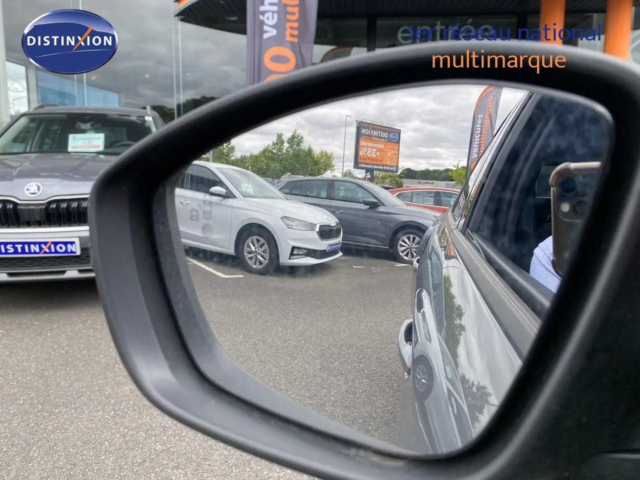 Rétroviseur montrant le côté droit d'une Peugeot 208 gris selenium metal en stationnement, reflet partiel du véhicule.