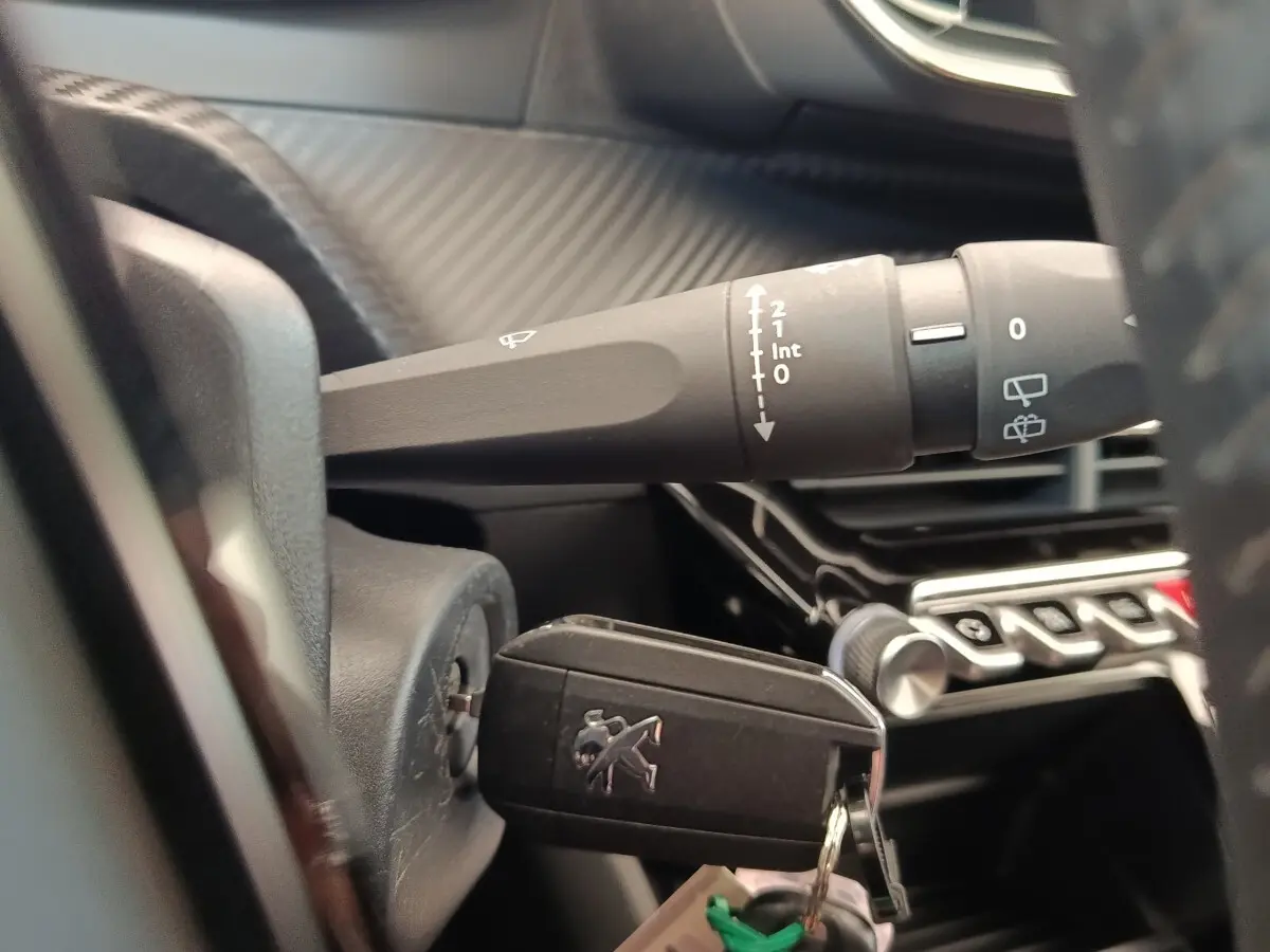 Gros plan intérieur sur la clé insérée dans le contacteur d'une Peugeot 208, avec commandes de phares et tableau de bord en arrière-plan.