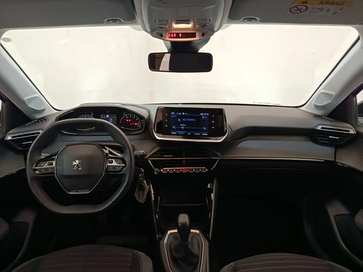 Vue intérieure frontale du tableau de bord noir de la Peugeot 208 PureTech 75 S&S Style avec écran tactile central et volant cuir multifonctions.