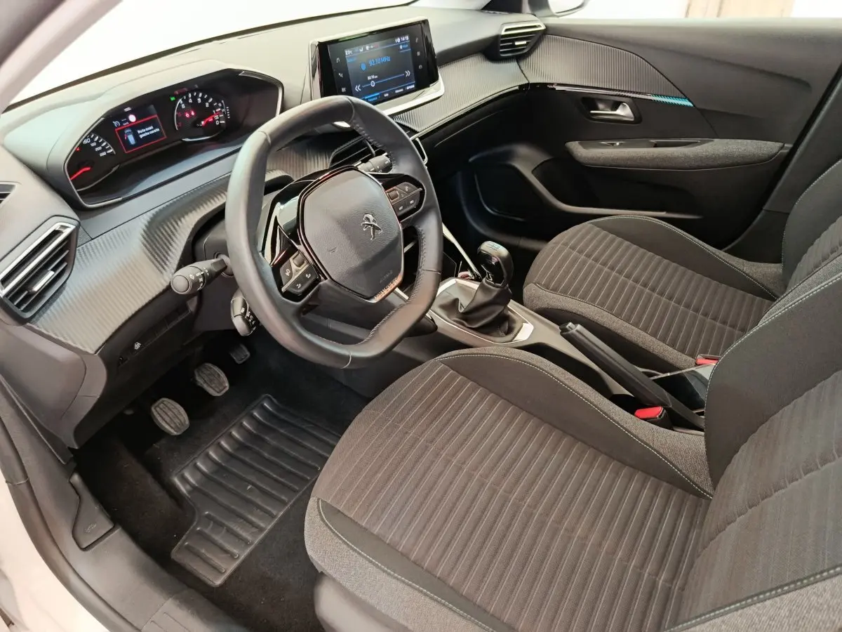 Vue intérieure côté conducteur de la Peugeot 208 PureTech 75 S&S Style 2023, volant cuir, tableau de bord moderne noir.